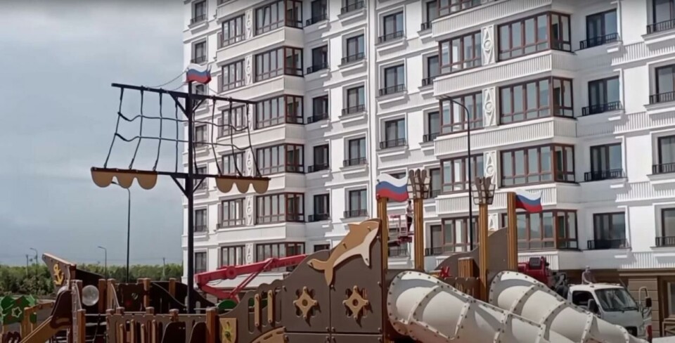 I bakgrunnen vises ett av de nye byggene. Legg merke til at det også er satt opp russiske flagg på lekeplassen. Skjermdump, YouTube