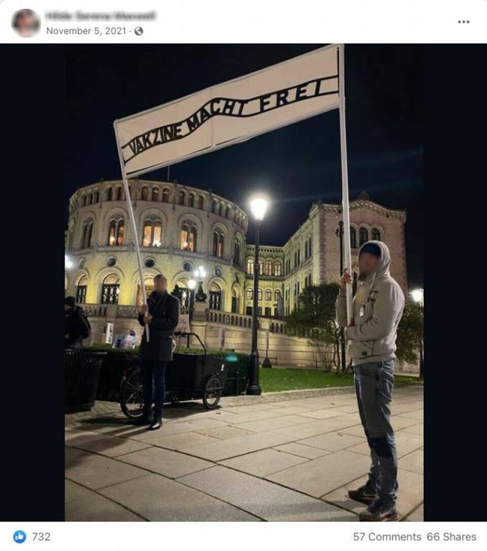 Flere har delt dette bildet av to menn utenfor Stortinget. Mellom seg holder de et banner med teksten «vakzine macht frei», som er en referanse til konsentrasjonsleire under krigen. Faktisk.no har anonymisert de to mennene. Skjermbilde: Facebook.
